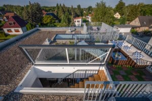 Lamilux zeigt eine Dachterrasse mit Sitzgelegenheiten, die über einen Treppenaufgang und ein großes Dachfenstern erreicht werden kann.