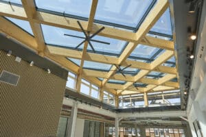 Lamilux zeigt eine große Glasdachfläche, die in Quadrate unterteilt und auf einer Holzkonstruktion montiert ist, von innen.