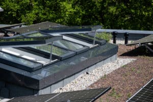 Lamilux zeigt ein schräges Dachfenster mit rechteckigen, teils geöffneten, Fensterflächen und dunkelgrauem Rahmen auf einem Flachdach.