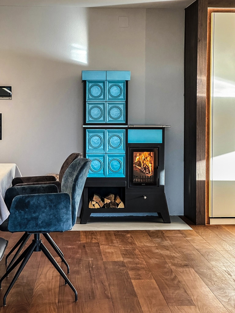 Klassischer Kachelofe mit hellblauen Reliefkacheln auf Standbeinen mit integriertem Holzlager von Ofenmanufaktur Liebewein in einem eleganten Esszimmer.