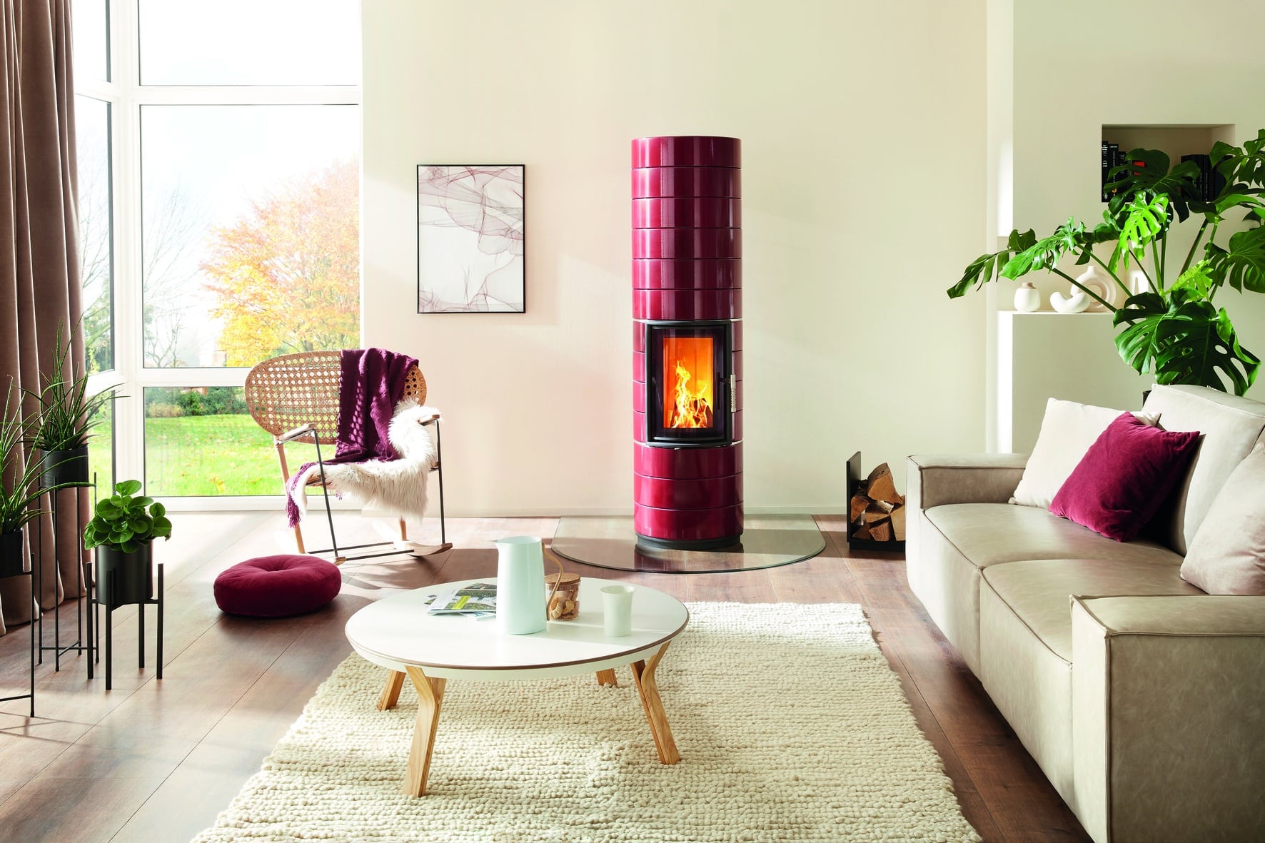 Moderner säulenförmiger Kachofen mit glänzend bordeaux roten Kacheln von Ofenmanufaktur auf einer halbkreisförmigen Glasplatte in einem helle Wohnzimmer.