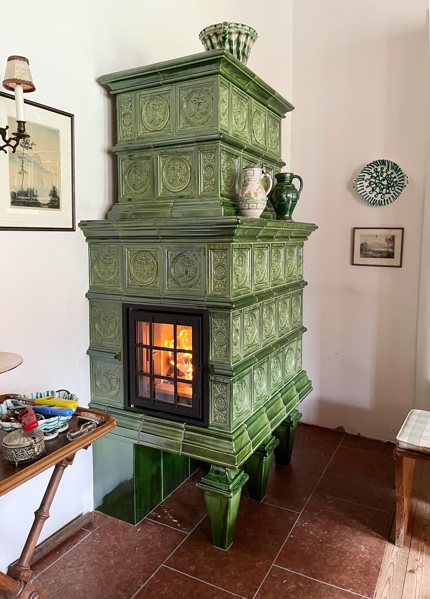 Klassischer Kachelofen mit grünen Relief-Kacheln und schwarzer Metall-Ofentüre mit Gitter von Ofenmanufaktur Liebewein.