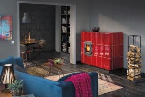 Speicherofen aus rot glänzenden Kacheln mit Türe aus Gusseisen von Ofenmanufaktur Liebewein in einem behaglichen Wohnzimmer mit dunklem Holzboden.