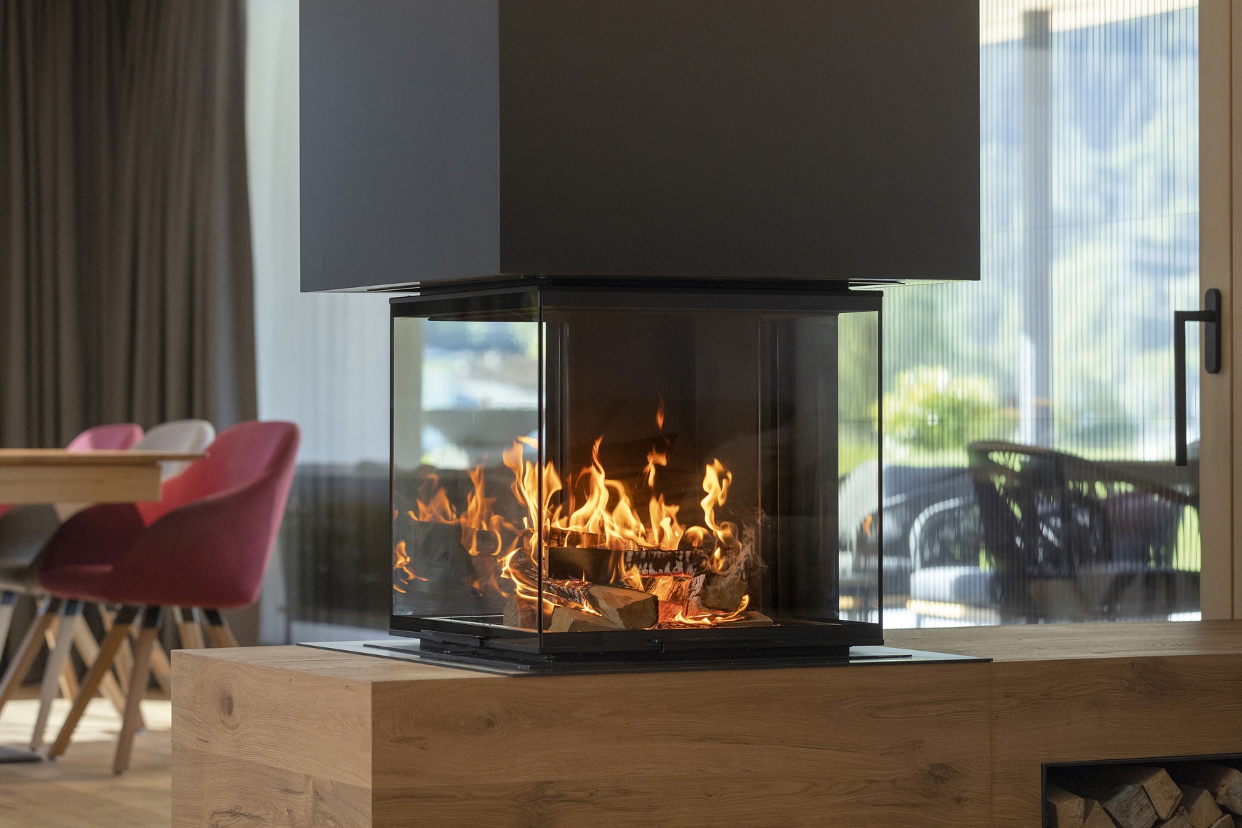 Schwarzer Kamin mit 4-seitiger Sichtscheibe auf Holzsockel von Ofenmanufaktur Liebewein.