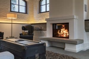 Weißer Speicherkamin mit Feuertisch aus grauem Stein, Ziegelsteinreihe über dem großen Sichtfenster von Ofenmanufaktur Liebewein.