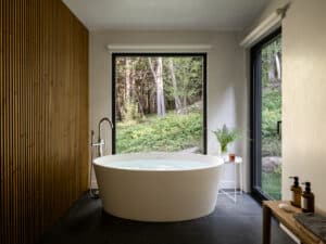 Modernes Badezimmer mit runder freistehender Badewanne, schwarzem Fensterrahmen, großer Fixverglasung und herrlichem Ausblick von M SORA.