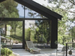 Terrassenansicht eines modernen Hauses in schwarzer Holzverkleidung mit Satteldach und passender Terrassenschiebetür und Fixverglasung von M SORA.