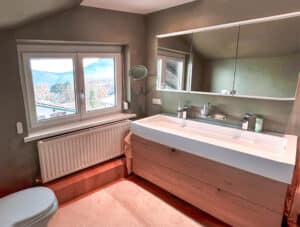 MANO Bad zeigt ein Badezimmer mit schwebendem Echtholz-Doppelwaschtisch, beleuchtetem Alibert, Vergrößerungsspiegel und moderner Eleganz.