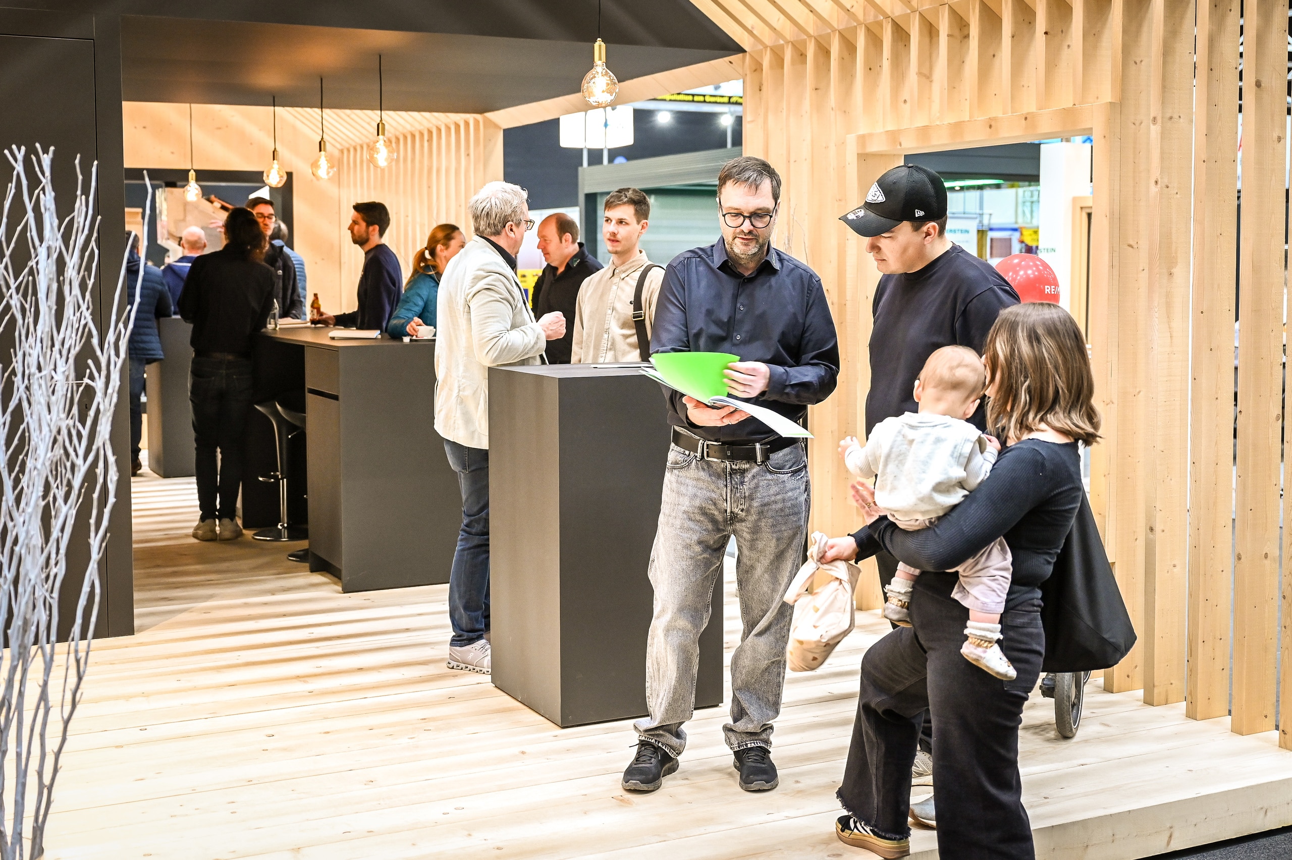 Ein offener Holzhaus-Rohbau mit Satteldach und Dachfenster als Ausstellungsstand mit fachkompetenter Bauberatung in der Messehalle Dornbirn auf der Baumesse "com:bau".