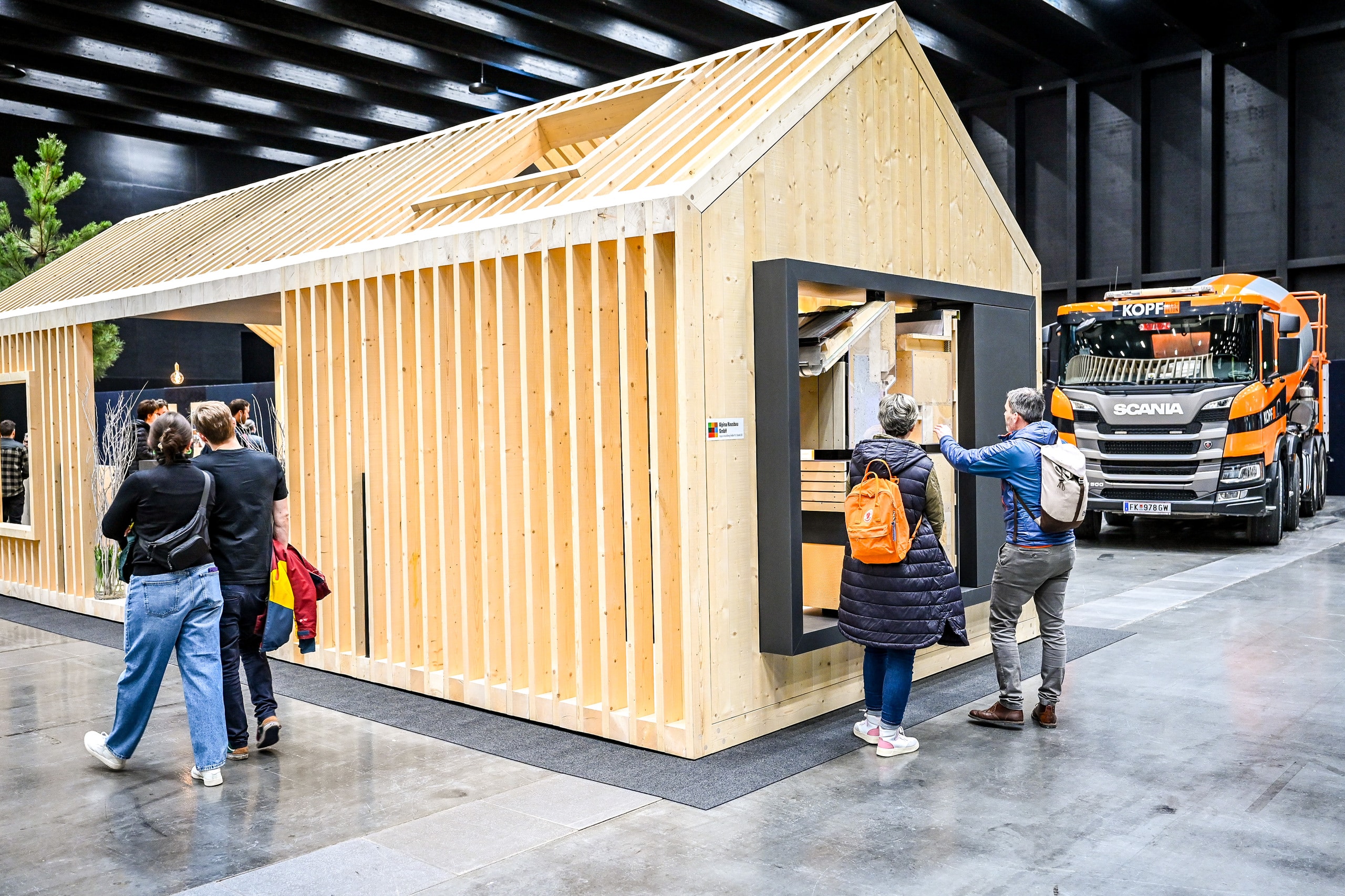 Ein offener Holzhaus-Rohbau mit Satteldach und Dachfenster als Ausstellungsstand in der Messehalle Dornbirn auf der Baumesse "com:bau".
