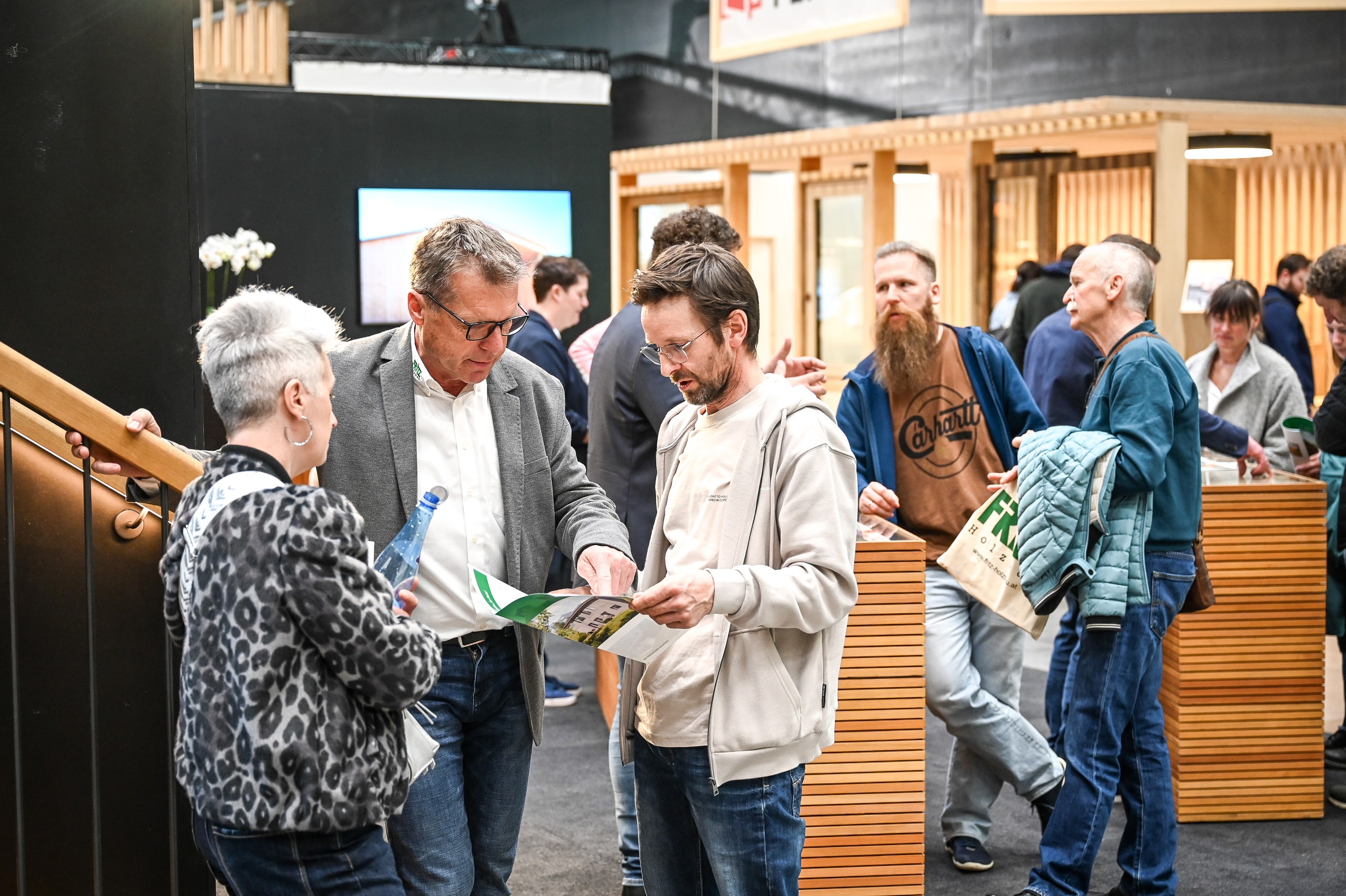Ein Beratungsgespräch zum Thema Hausbau an einem Messestand der Messe com:bau mit Informationsunterlagen und Planungsmaterialien, bei dem Fachberater Besucher zu Planung, Umsetzung und Finanzierung eines Eigenheims informieren.