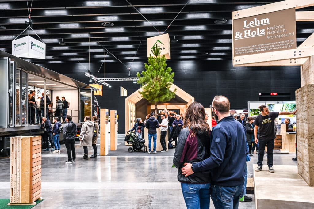 Ein Paar beim Rundgang durch eine Ausstellungshalle der Baumesse com:bau zwischen Informationsständen und Ausstellern zu Bau-, Wohn- und Einrichtungsthemen im Messequartier Dornbirn. Die com:bau bündelt Bauwirtschaft, Fachleute und Interessierte an einem Ort und bietet unabhängige Beratung zu Sanierung, Bau, Energieplanung und Finanzierung.