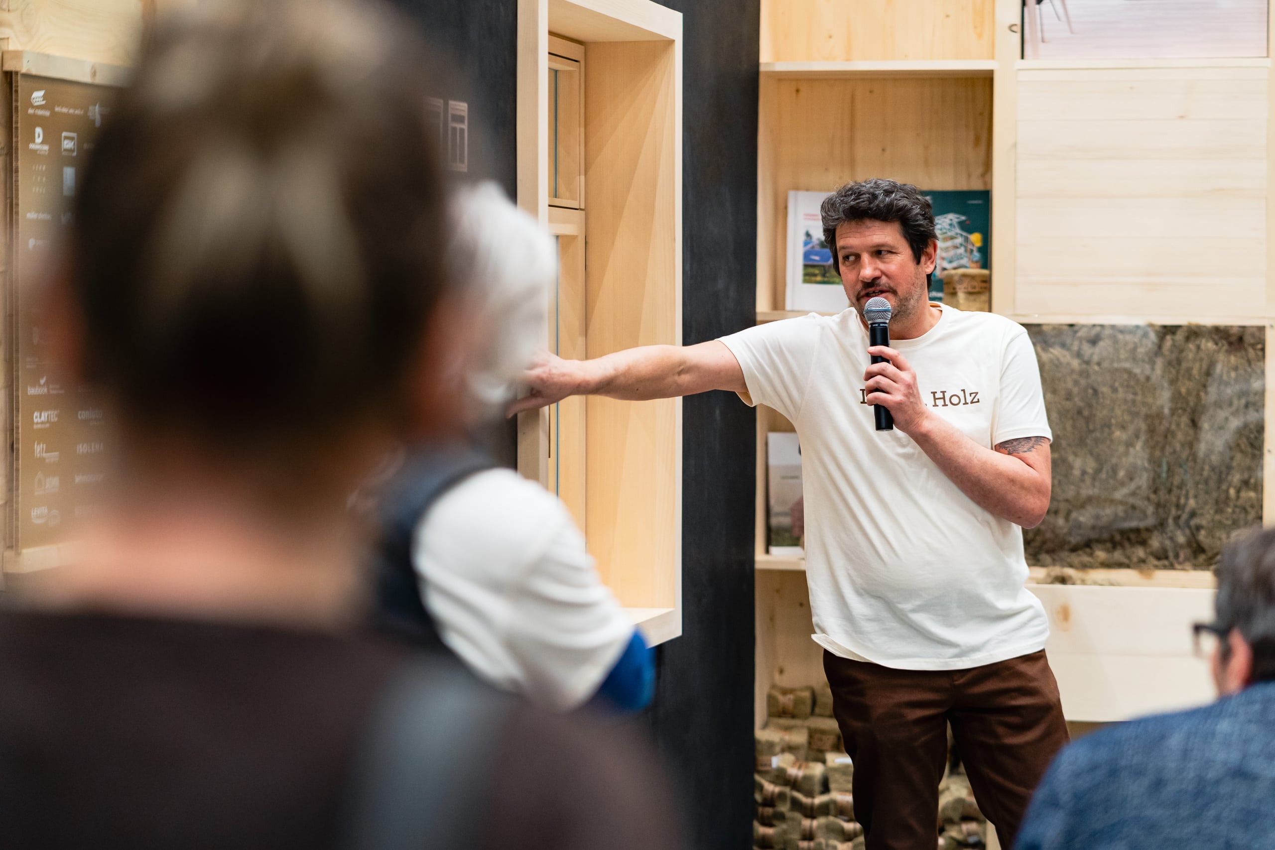 Ein Fachvortrag bzw. Beratungsgespräch zum Thema Holzbau vor einem Publikum an einem Informationsstand auf der Baumesse com:bau im Messequartier Dornbirn.