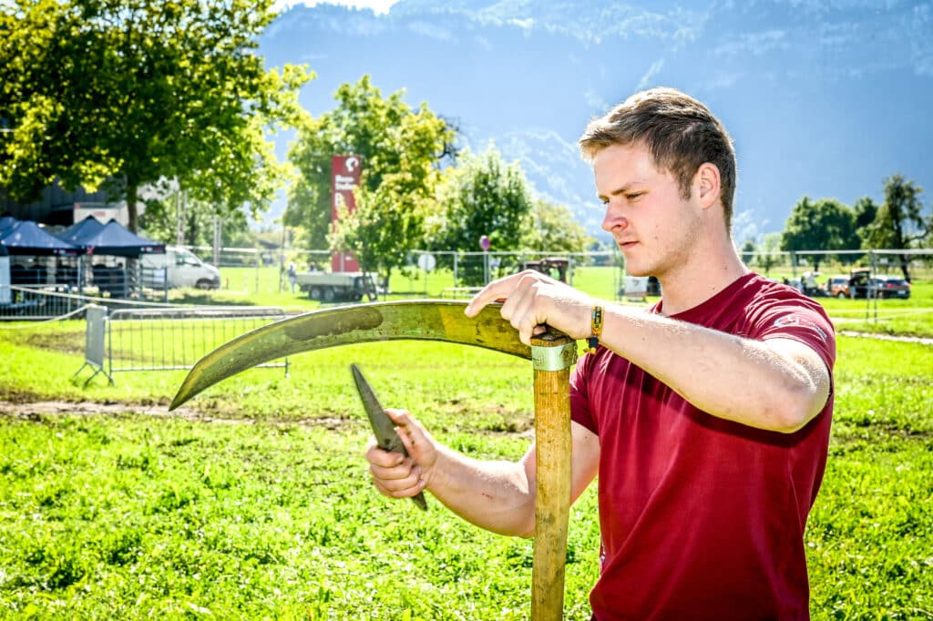 Die Herbstmesse Dornbirn zeigt Einblicke in echte regionale, forstwirtschaftliche Handwerksberufe - hier ein junger Mann beim Schleifen einer Sense.