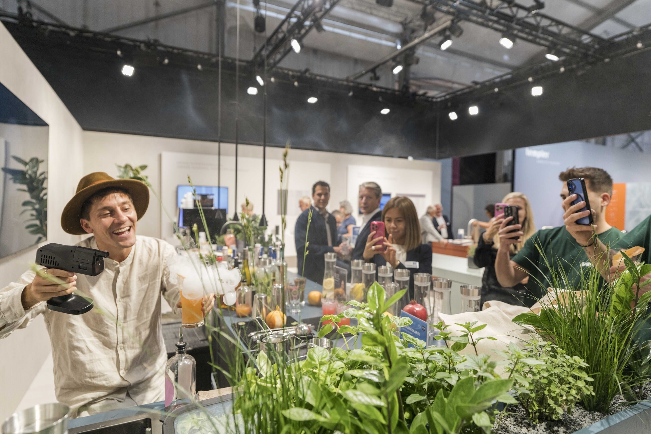 In einer Schauküche mit Kräuterbepflanzung wird auf der Fachmesse area30 ein Cocktailglas mit einer Rauchpistole beschossen.