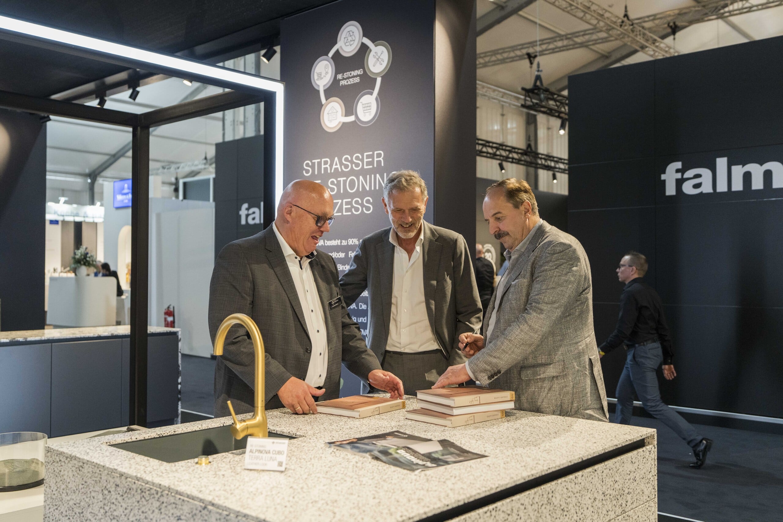 Drei Männer überblicken in einer Schauküche die verschiedenen Muster von langlebigen Steinarbeitsplatten auf der Fachmesse area30.