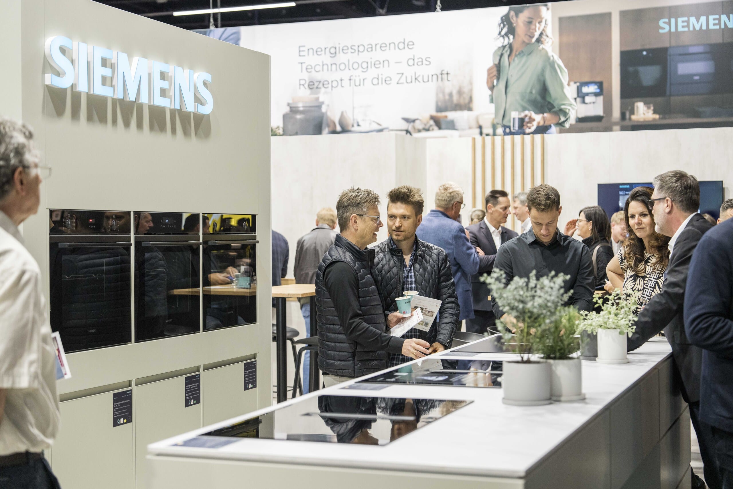 Schauküche mit drei verschiedenen Backöfen und Ceranfeldern und interessierten Besuchern auf der Messe "küchenwohntrends".