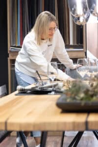 Eine Frau betrachtet Gedeck und Stoffmuster an einem Essbereichs‑Ausstellungsstand auf der Energiesparmesse Wels.