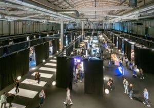 Die Messe ARCHITECT@WORK Wien zeigt die Messehalle von Innen mit den Kojen der Ausstellern und Tischen, die Platz für Besprechungen bieten.