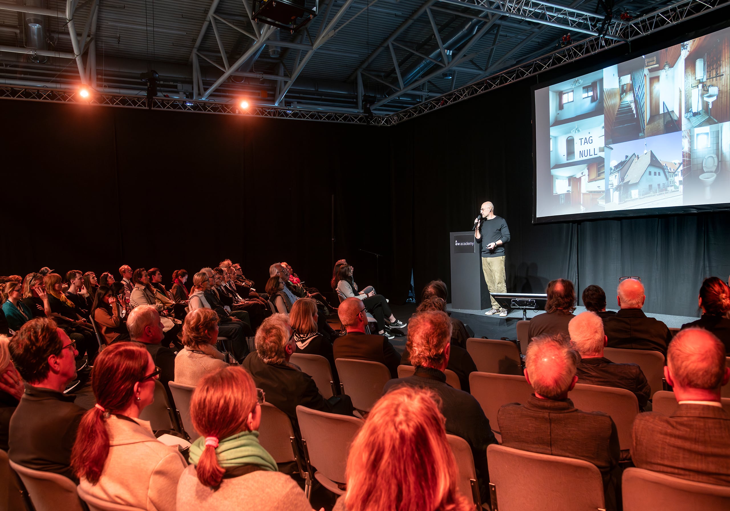ARCHITECT@WORK Messe Wien 2026 zeigt einen Vortrag in einem großen Saal mit vielen Sitzreihen, einer Bühne mit Leinwand und Pult.