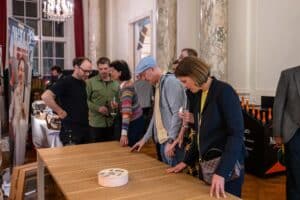 Besucher der Messe Design District 1010 begutachten einen hochwertigen Esstisch mit gerillter Oberflaeche aus Holz.