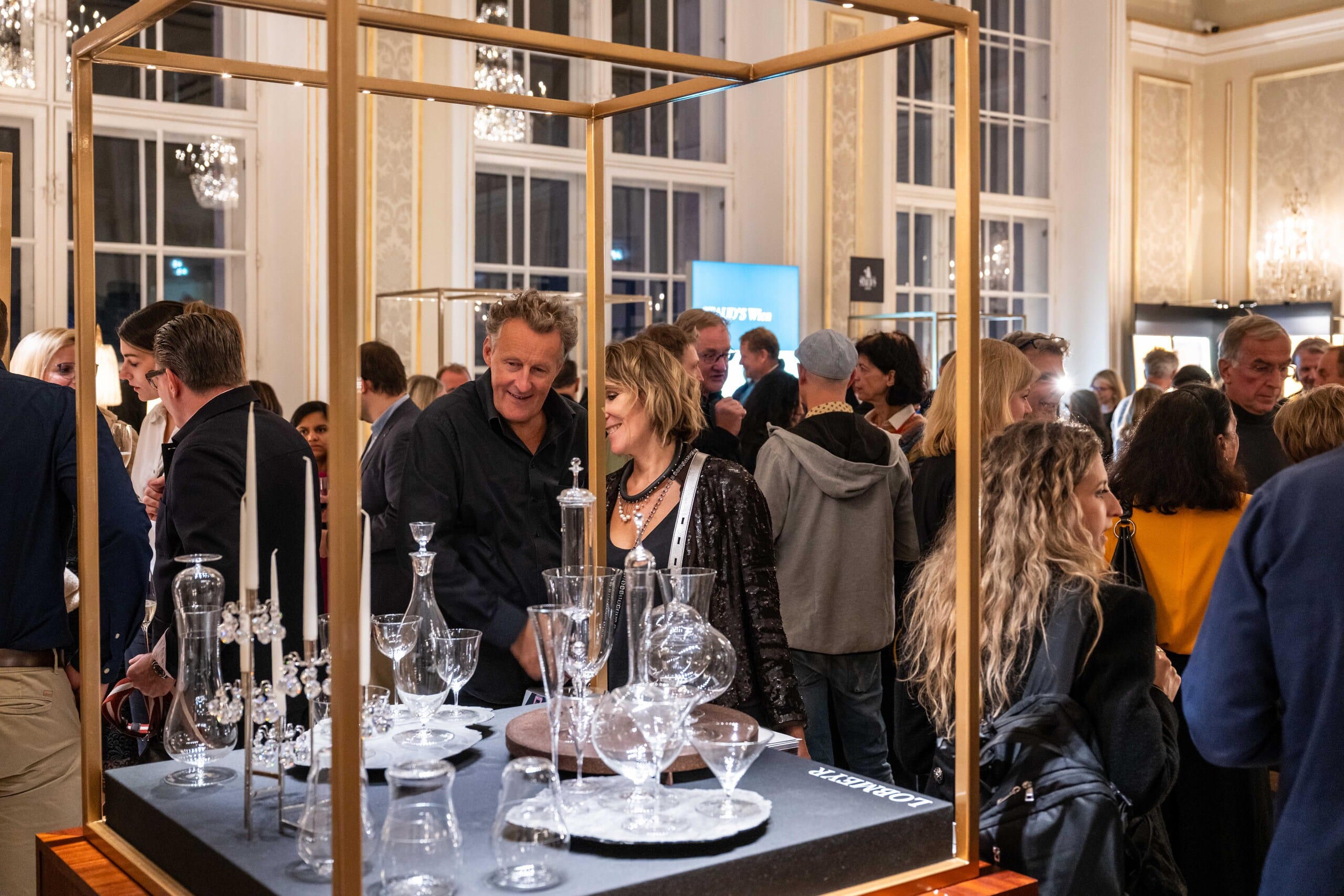 Besucher der Messe Design District 1010 betrachten hochwertiges Geschirr und elegante Gläser in stilvoller Präsentation.