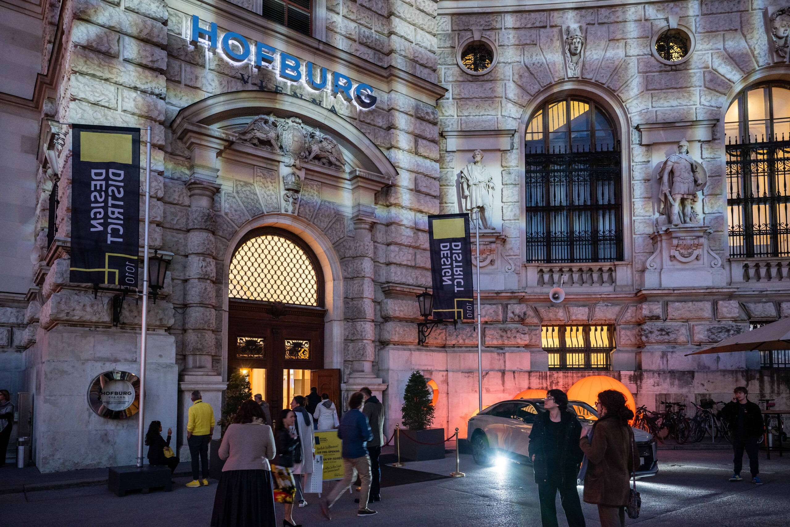 Besucher der Messe Design District 1010 passieren das Eingangstor zum Außenbereich der Wiener Hofburg nach Abendeinbruch.