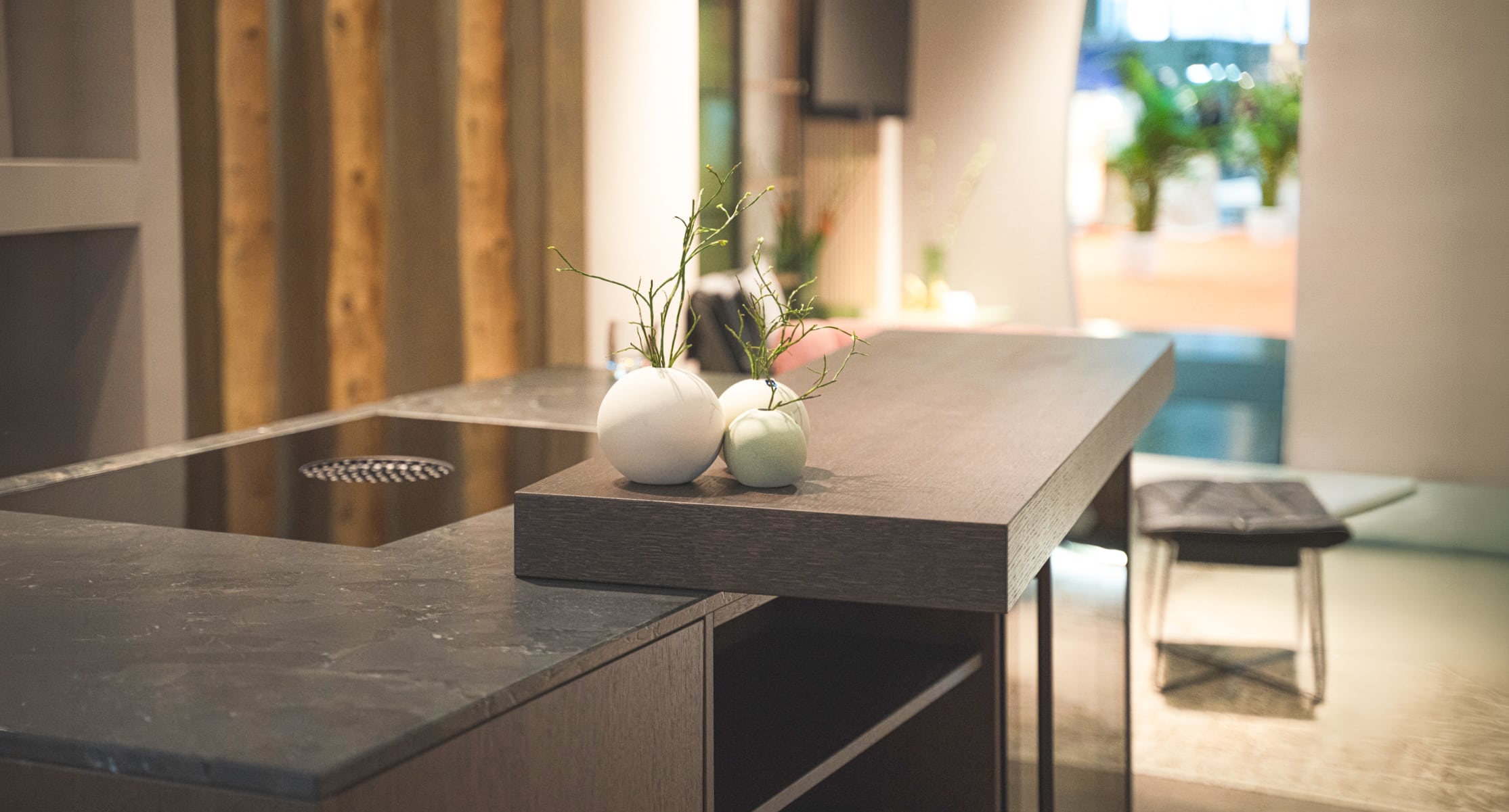 Eine Kücheninsel mit dunkler, schräg versetzt aufgelegter Holztheke, mattschwarzer Marmorarbeitsfläche und integriertem Induktionsfeld auf der Wohnen & Interiour Messe von Austrian Exhibition Experts.