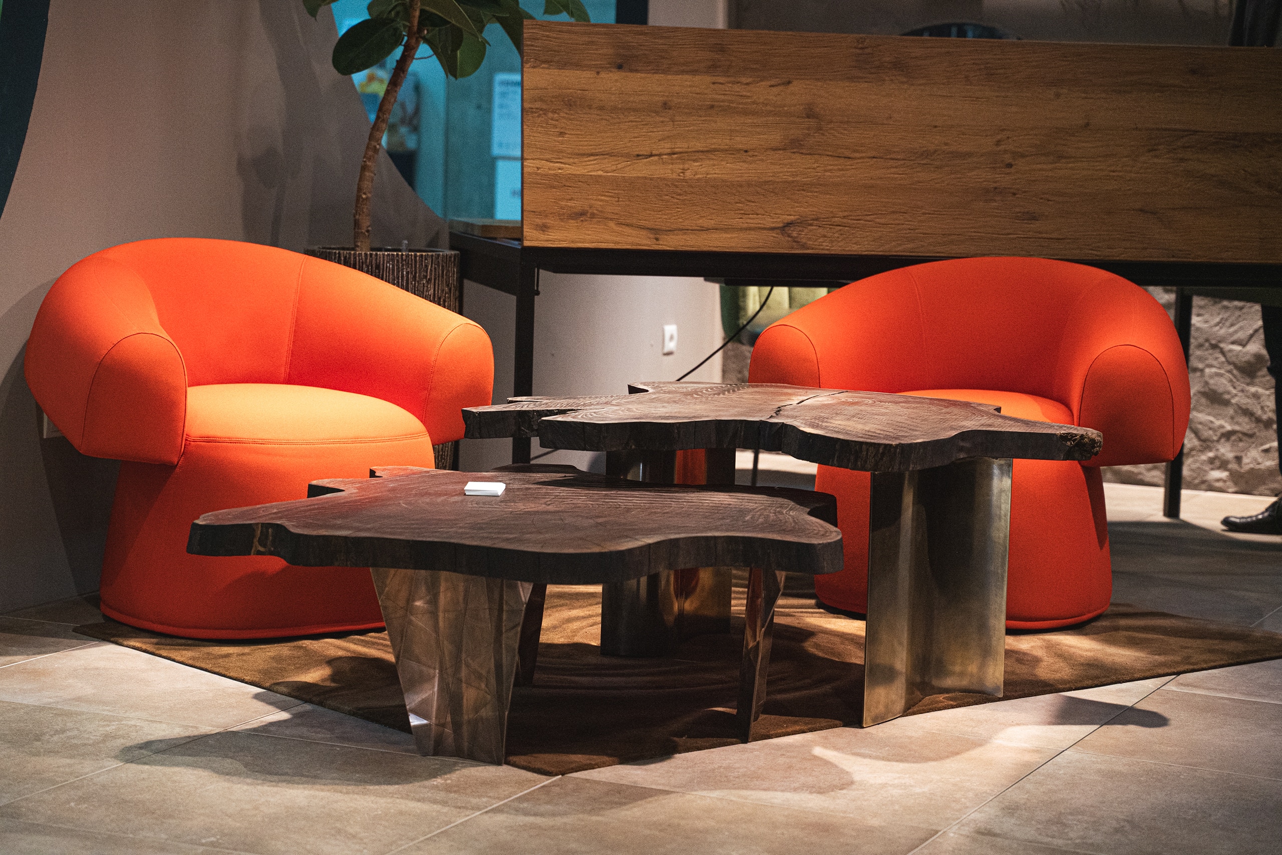Zwei orangefarbene moderne Ohrensessel mit kunstvollen Holztischen stehen in einer Lounge‑Inszenierung auf der Messe Wohnen & Interieur.