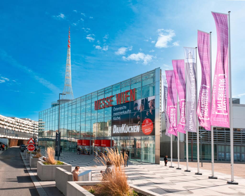 Das moderne VIECON-Messegelände in Wien mit Glasfassade und den pinken Fahnen der Austrian Exhibition Experts Messe Wohnen & Interieur.