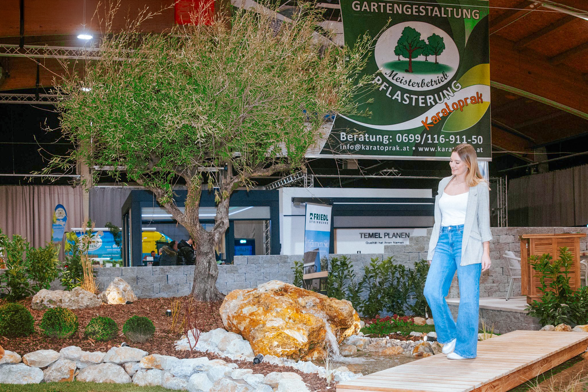Eine Frau in der Messehalle der Arena Nova Haus & Garten-Messe in einem Ausstellungs-Gartenobjekt mit Steinbrunnen.
