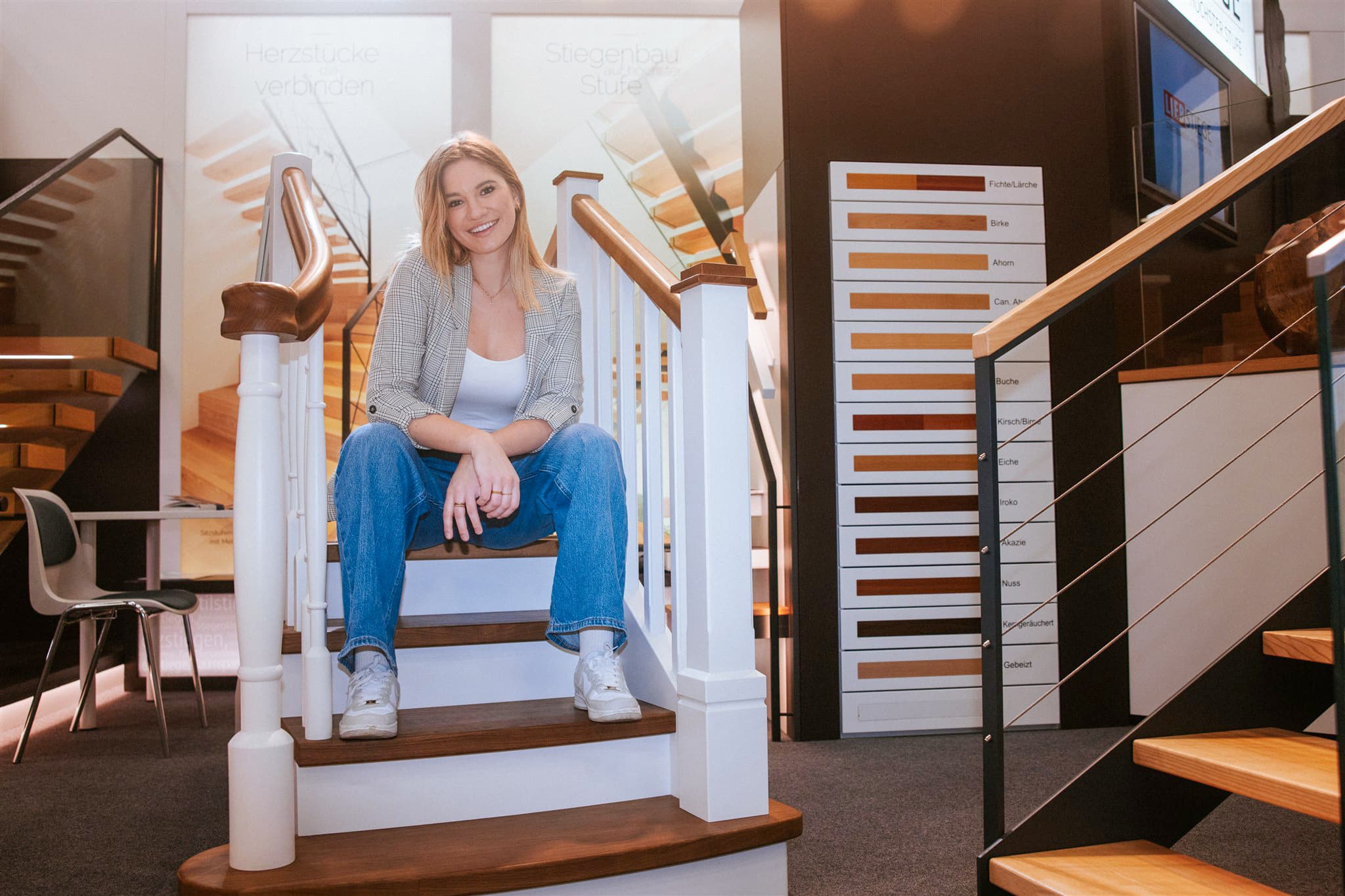 Eine Frau sitzend auf einer ausgestellten Holztreppe, umgeben von weiteren Treppen- und Stiegenmustern auf der Haus & Garten-Messe in der Arena Nova Wiener Neustadt.