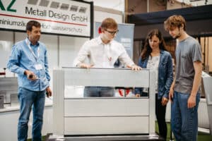 Vier Personen betrachten ein modernes Aluminiumelement an einem Stand eines Metallbauunternehmens auf der Messe Wieselburg.