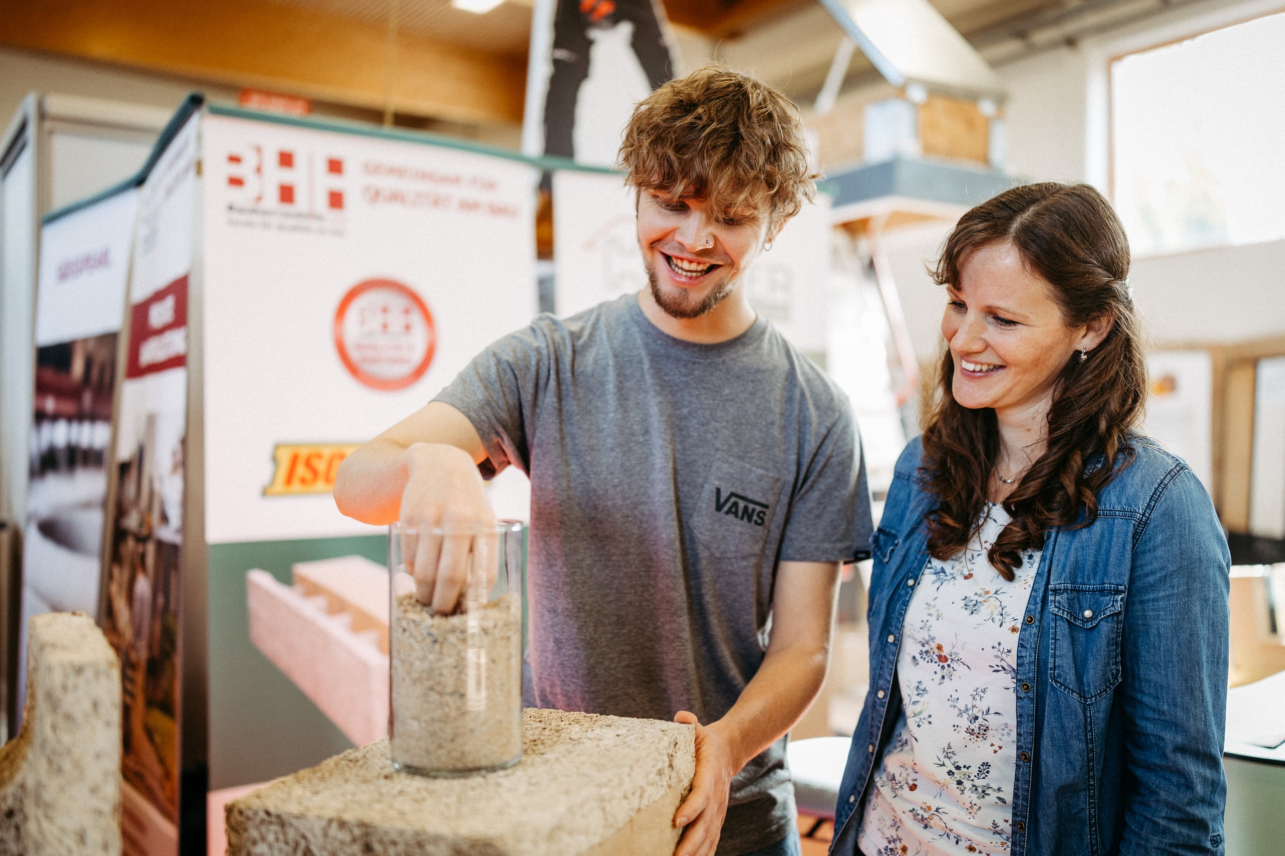 Ein junger Mann und eine Frau betrachten lächelnd ein Baumaterial-Muster und testen dessen Beschaffenheit mit der Hand auf der Messe Wieselburg.