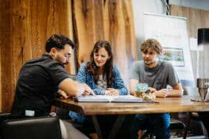 Drei Personen sitzen an einem Holztisch und besprechen gemeinsam Materialmuster und Designideen in entspannter Atmosphäre auf der Messe Wieselburg.
