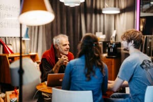 Ein älterer Mann führt an einem kleinen Tisch mit Laptop ein Beratungsgespräch mit zwei jungen Besuchern in gemütlicher Atmosphäre auf der Messe Wieselburg.