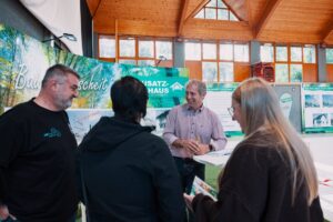 Besucherinnen und Besucher im persönlichen Gespräch über individuelle Möglichkeiten der Hausplanung mit "Bausatzhaus" auf der Messe Bau.Energie.Wohnen in Wieselburg.