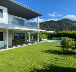 Ein moderner Sommergarten mit weißer Markise und darunterliegender Pergola mit großzügigen Glas-Schiebeelementen und lichtdurchfluteter Gestaltung, der einen flexiblen und wettergeschützten Übergang zwischen Haus und Garten schafft von Moltke.