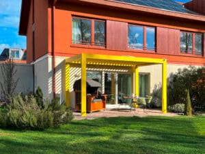 Einfamilienhaus mit roten Fassadenelementen und einer Terrasse mit einer fassadenmontierten knall-gelben Lamellenpergola.