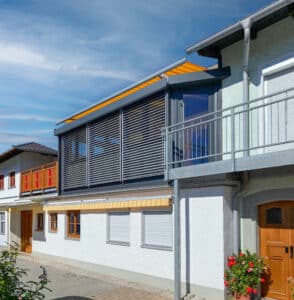 Ein moderner Wintergarten im Obergeschoss mit Außenjalousien und einer orange-gelb-gestreiften Markise von Moltke.