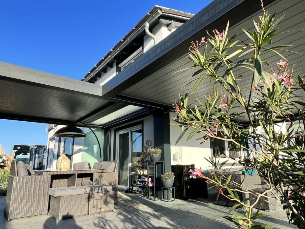 Eine moderne L-förmige Lamellenpergola in Anthrazit mit stabiler Eckkonstruktion, verstellbarem Lamellendach und harmonischer Integration in die Haus- und Terrassengestaltung für einen geschützten Außenbereich von Moltke.