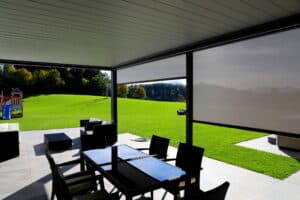 Eine moderne Pergola mit Lamellendach in Anthrazit und halboffenen grauen Seitenmarkisen, ausgestattet mit stilvollen Outdoor-Möbeln, die einen komfortablen und geschützten Wohnbereich im Garten schafft und zum Entspannen im Freien einlädt - von Moltke.