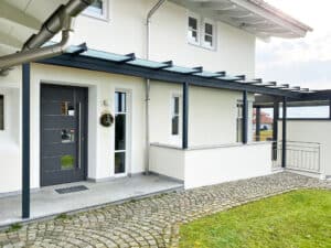 Ein moderner Hauseingang mit elegantem satinierten Glasvordach, im Pergola-Stil mit anthrazitfarbener Rahmenkonstruktion von Moltke.
