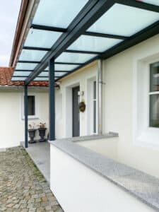 Ein moderner Hauseingang mit elegantem satinierten Glasvordach, im Pergola-Stil mit anthrazitfarbener Rahmenkonstruktion von Moltke.