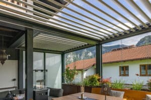 Ein Wintergartenanbau in Anthrazit mit halboffenem Lamellendach und seitlich geschlossenen Glasschiebetüren von Moltke.