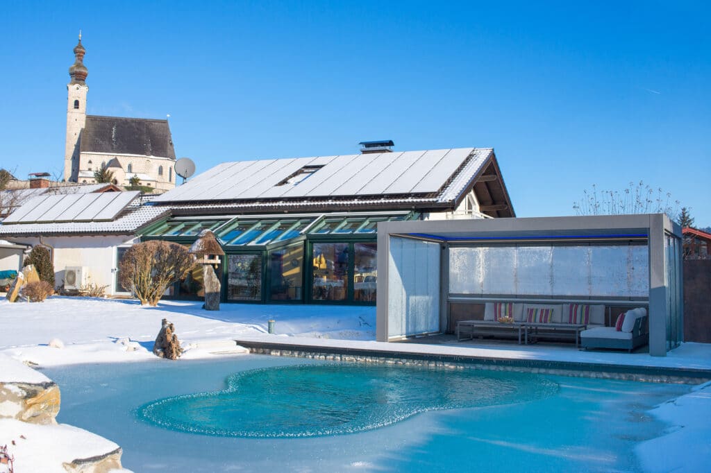 Ein moderner Garten in winterlicher Atmosphäre und gefrorenem Biotop-Teich mit Pergola, Lamellendach und an drei Seiten geschlossenen Glasschiebetüren von Moltke.