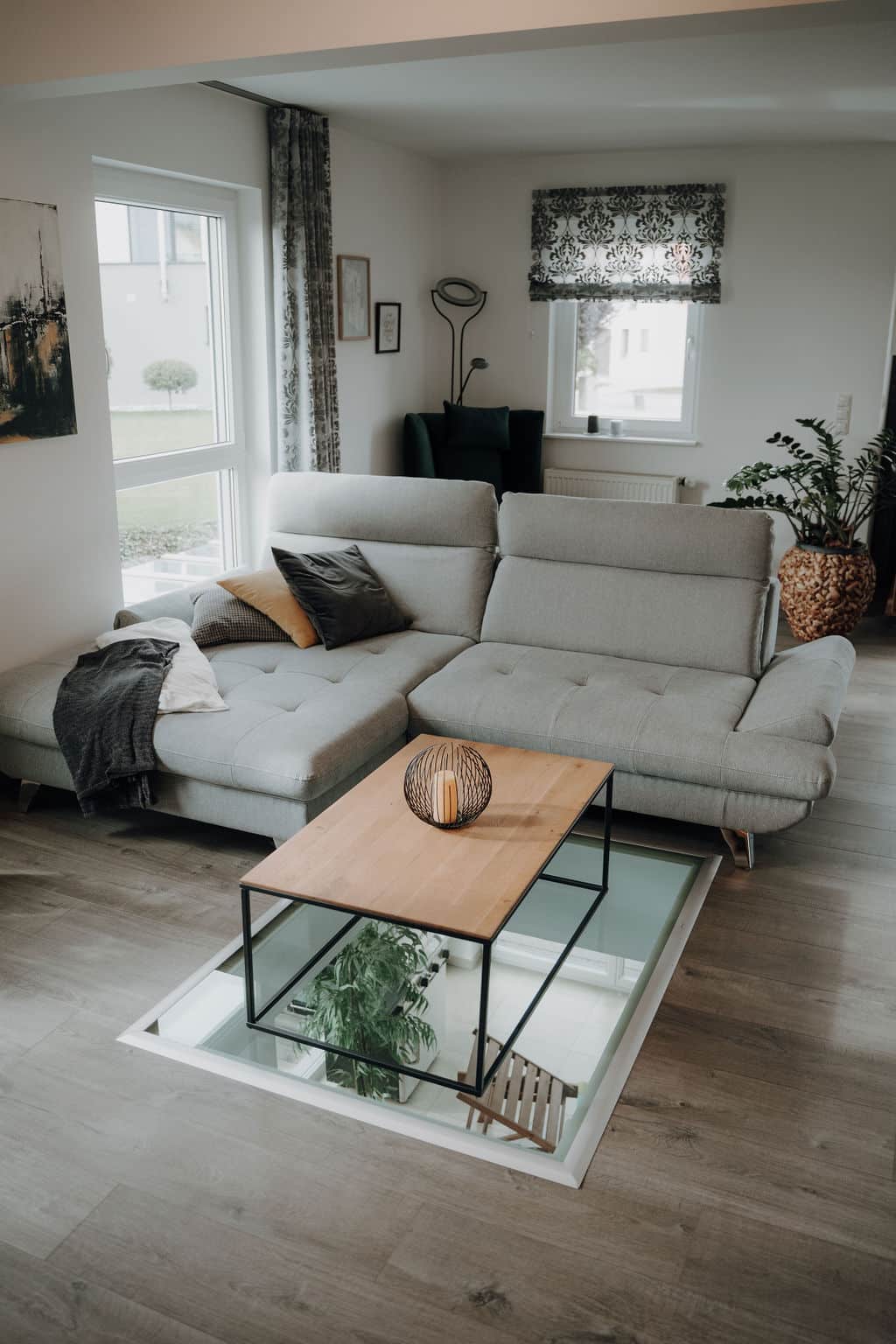 Wohnzimmer mit gemütlichem Sofa, Tür zur Terrasse und als besonderes Highlight ein Bodenfenster mit Sicht in den Wohnkeller im Musterhauspark.