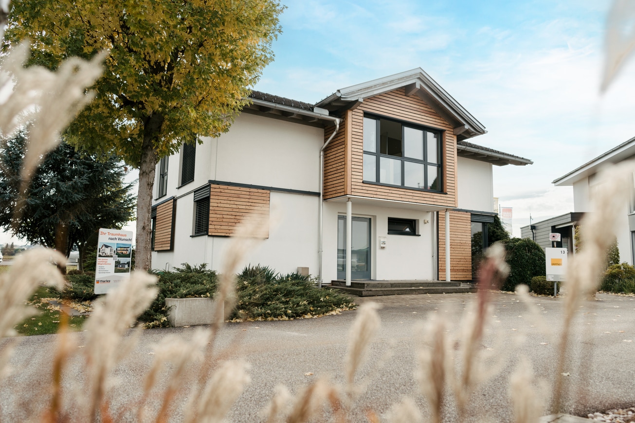 Einfamilienhaus mit Zwerchdach welches gleichzeitig als Vordach zum Eingangsbereich dient und Fassadenelementen und Fensterschiebeläden aus Holz im Musterhauspark Haid.