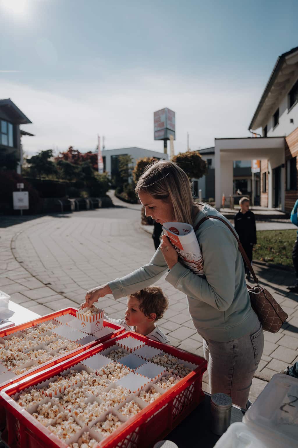 Eine junge Mutter mit kleinem Kind bedienen sich am Popcornstand der Hausmesse des Musterhausparks.