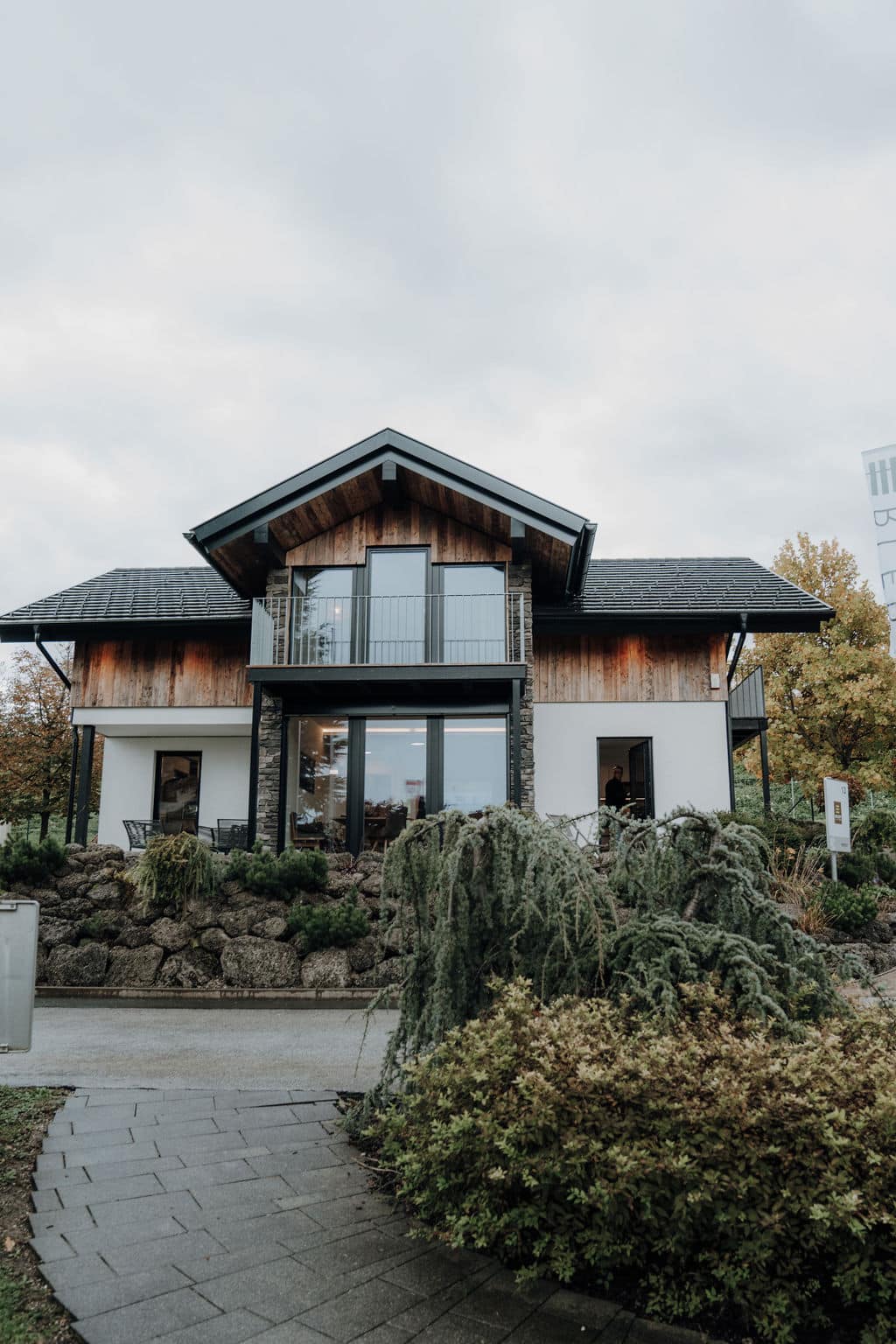 Musterhaus mit Zwerchdach, Balkon, überdachter Terrasse und einem Fassadenmix aus Beton, Holz und Stein im Musterhauspark.